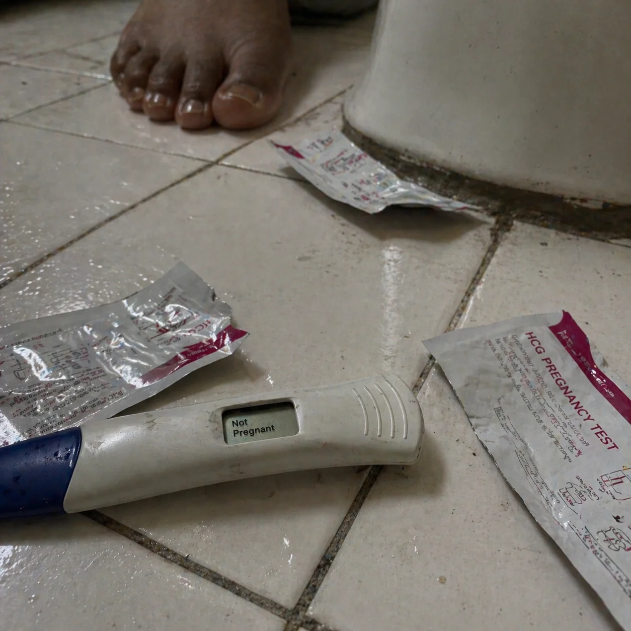 Three pregnancy test wrappers on a bathroom floor, digital test showing Not Pregnant