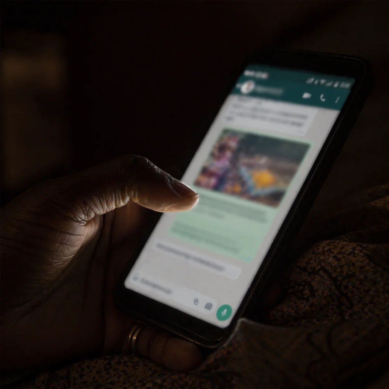 A woman's thumb hovering over a WhatsApp link in a dark bedroom