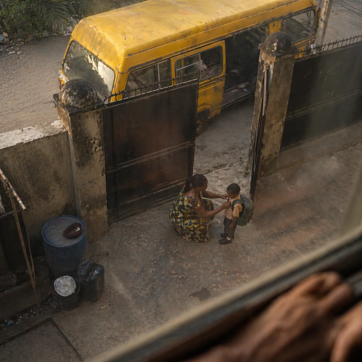 A mother adjusting her son's collar at the gate as the school bus waits