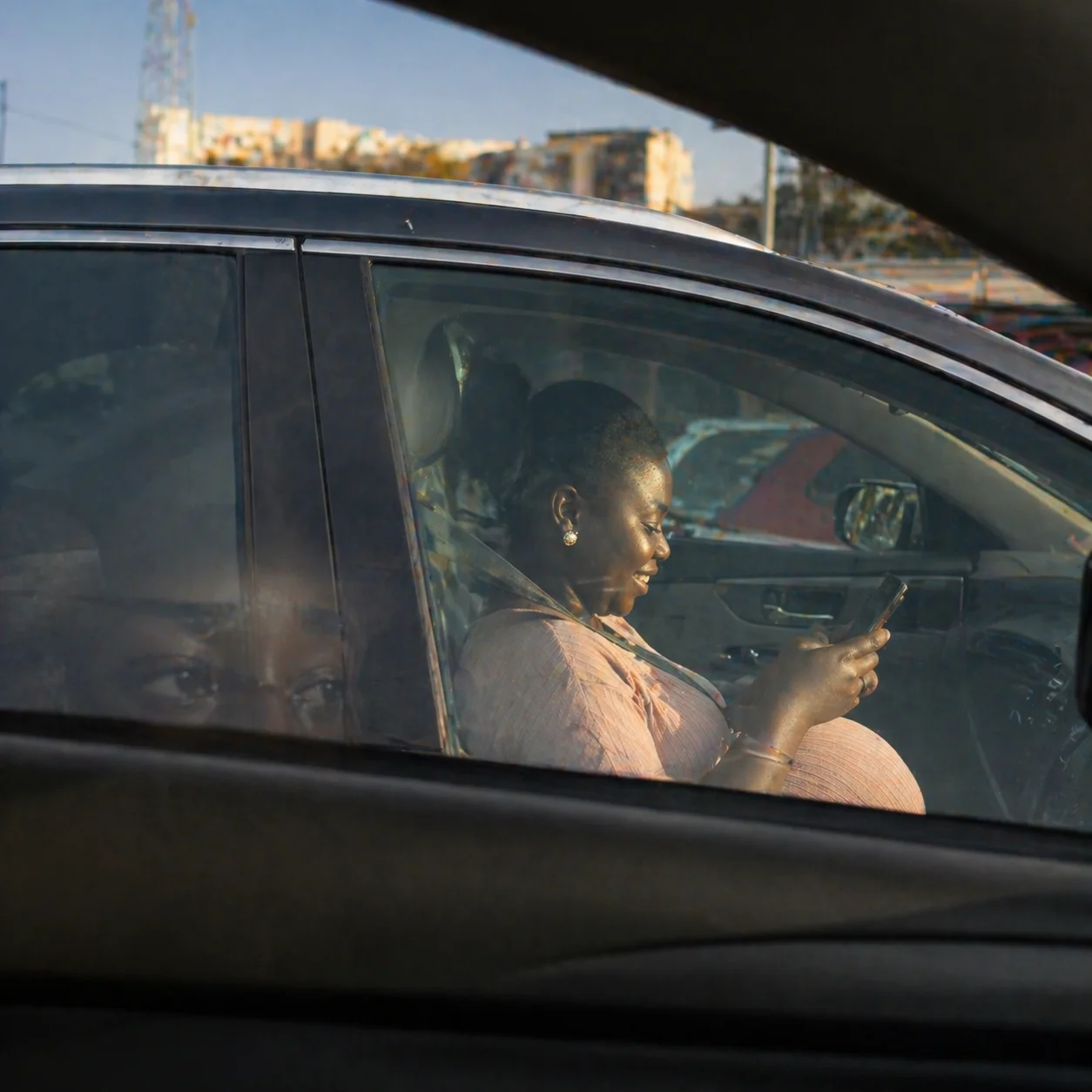 A heavily pregnant woman laughing in the car beside Adaeze, Adaeze's reflection in the glass